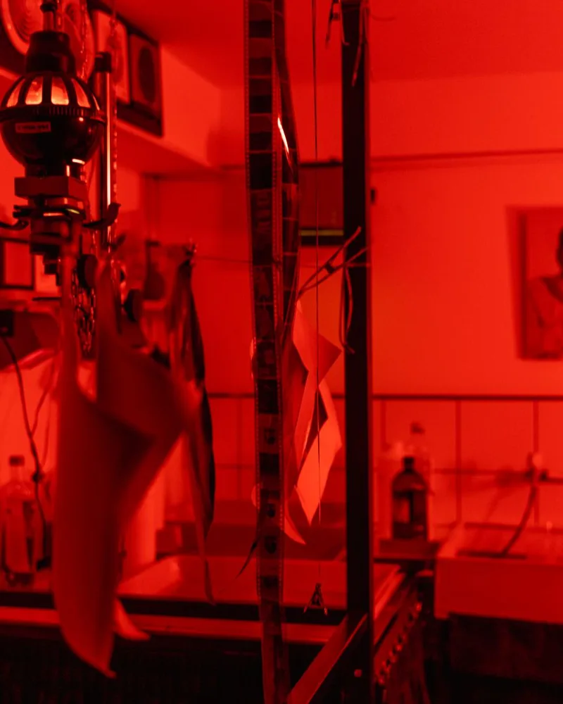 Tiras de negativos colgadas para secar junto al equipo de revelado en un laboratorio con luz roja